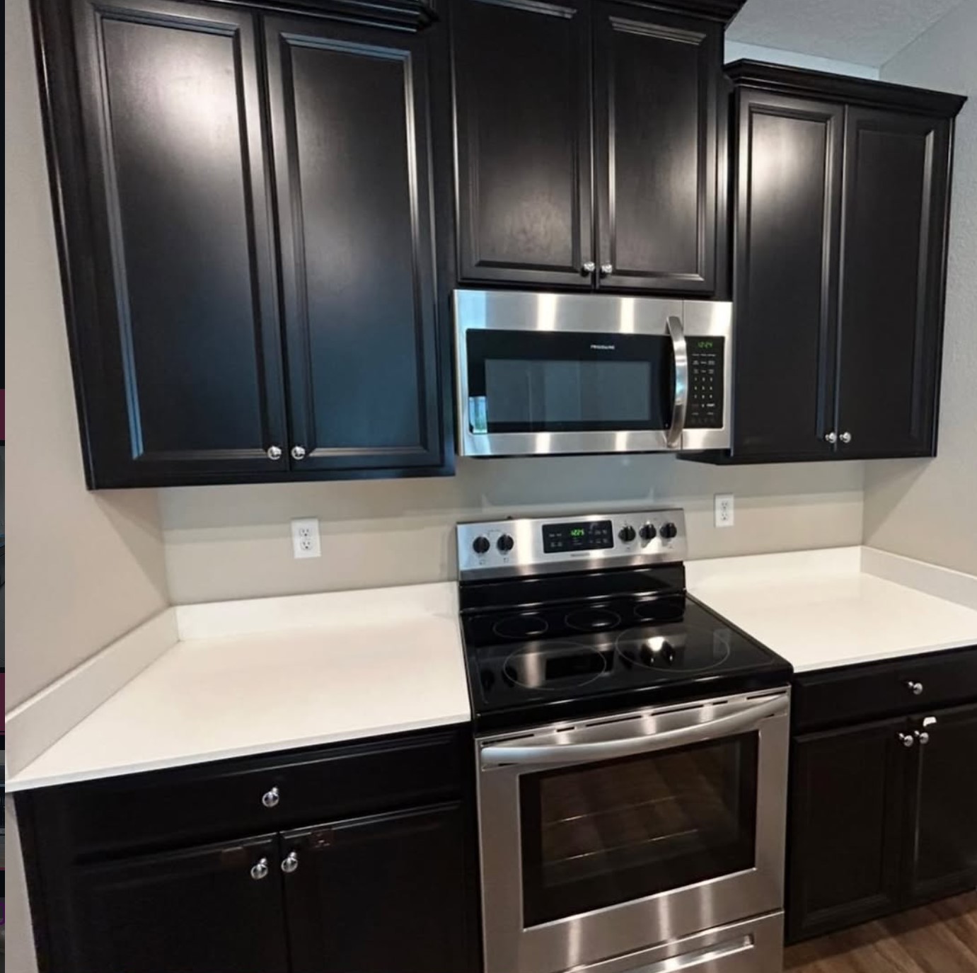 Clean kitchen with dark cabinets, stainless steel range and microwave, and wiped white countertops